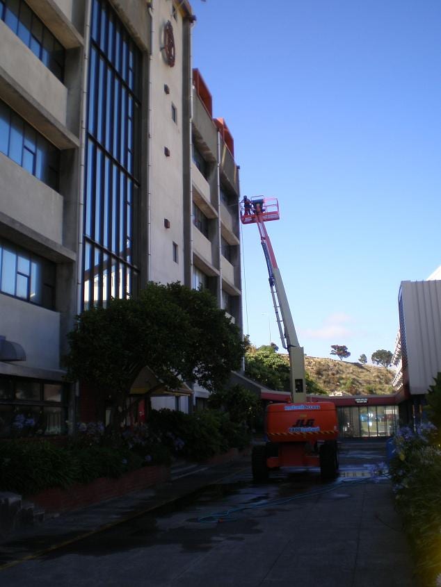 Wellington commercial cleaning at the Royal New Zealand Police College in Porirua, large JLG boom lift extended into the central courtyard to softwash atrium glazing and upper concrete bands at height.