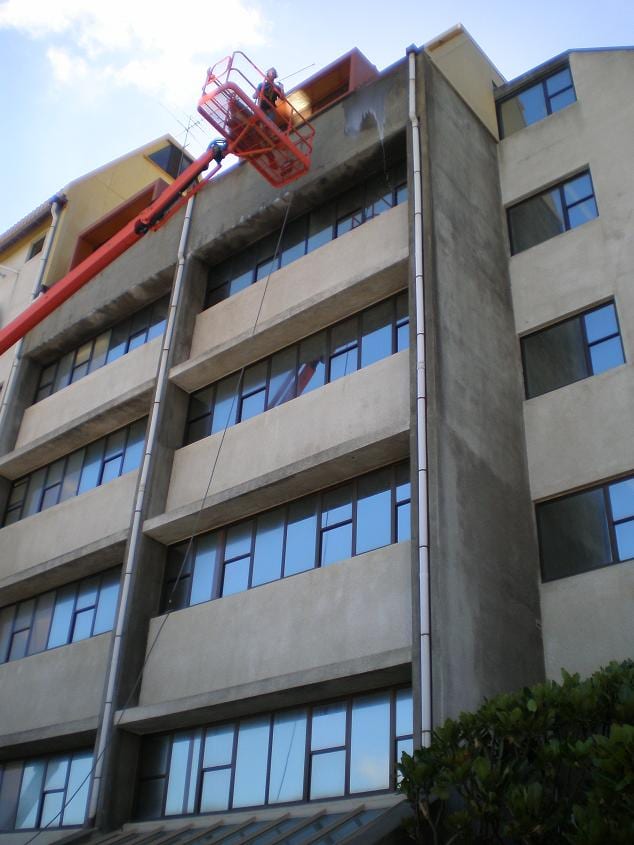 Wellington commercial cleaning at the Royal New Zealand Police College in Porirua, operator in a cherry picker softwashing a multi storey accommodation block at height, working dirt streaks down the concrete and glass facade.
