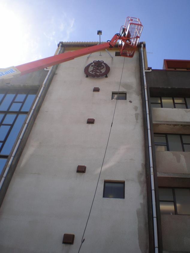 Wellington commercial cleaning at the Royal New Zealand Police College in Porirua, boom lift platform working below the police crest tower, lifting weathering streaks from the rendered facade with controlled low pressure rinse.