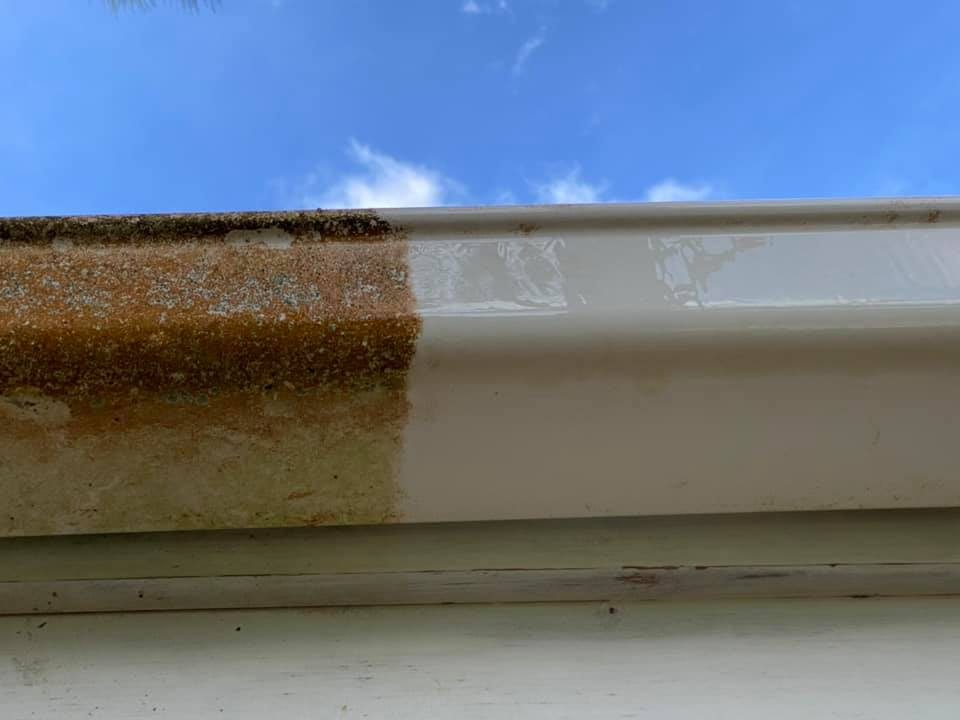 Gutter cleaning in Wellington, close-up of a single gutter panel mid-clean, the left half heavily stained with rust-orange grime and lichen, the right half cleaned to bright white