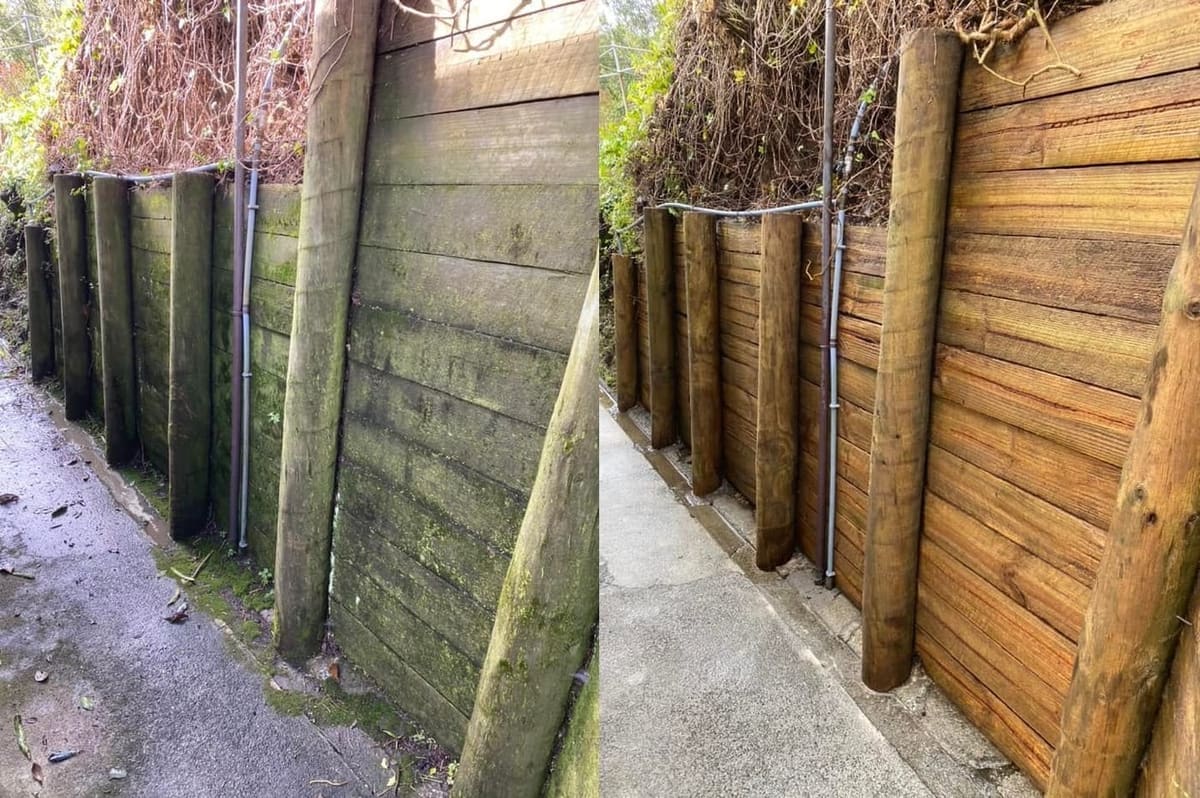 Wellington retaining wall cleaning before and after, mossy pole-and-sleeper timber retaining wall along a driveway before, fresh warm-toned timber after a high-pressure clean